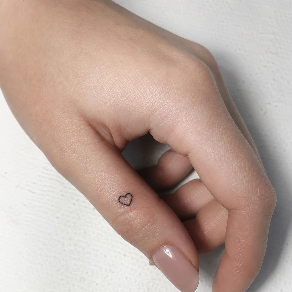 women's finger tattoo tiny heart, realistic photo on skin